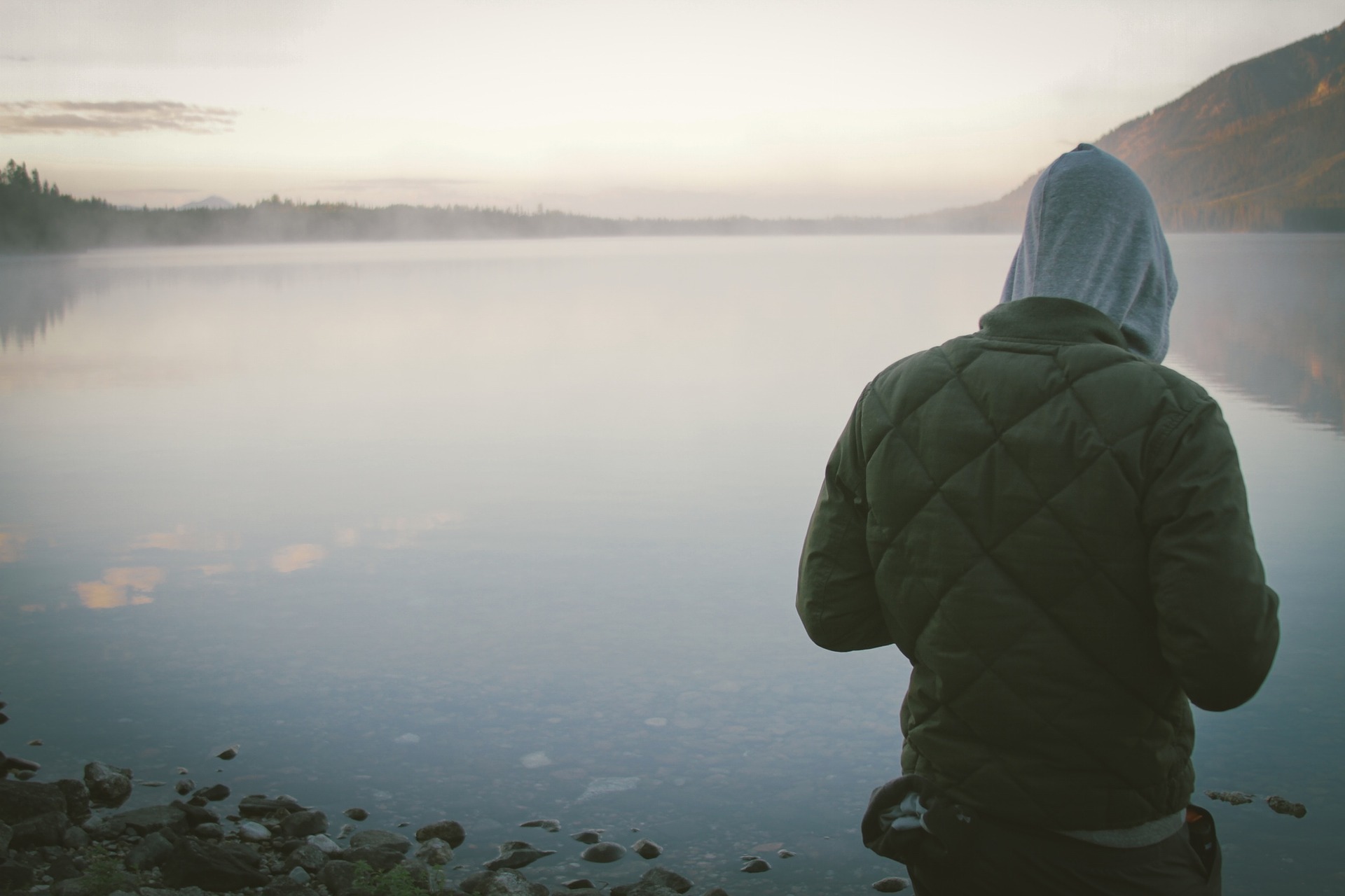 Alan Walker - Alone. A person dressed in a hoody turning with his back to us, appears from waist to head on the background of a big lake/sea