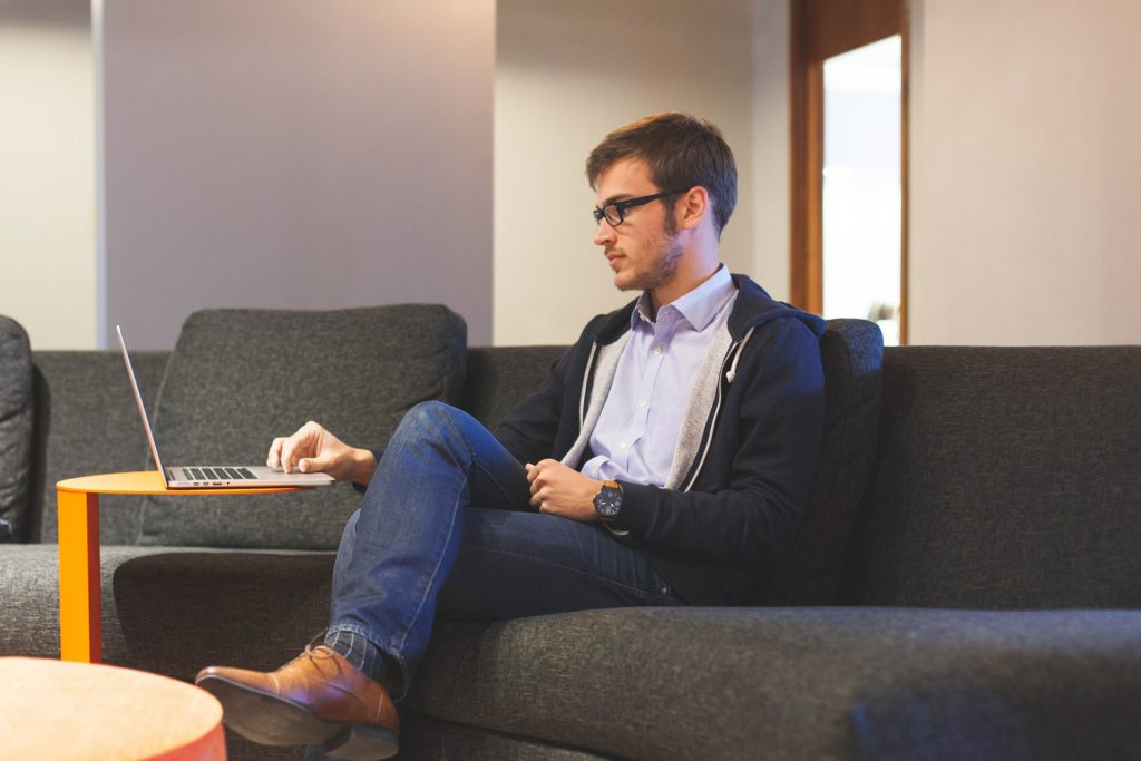 Formally dressed guy sitting on a couch with legs crossed and uses a laptop